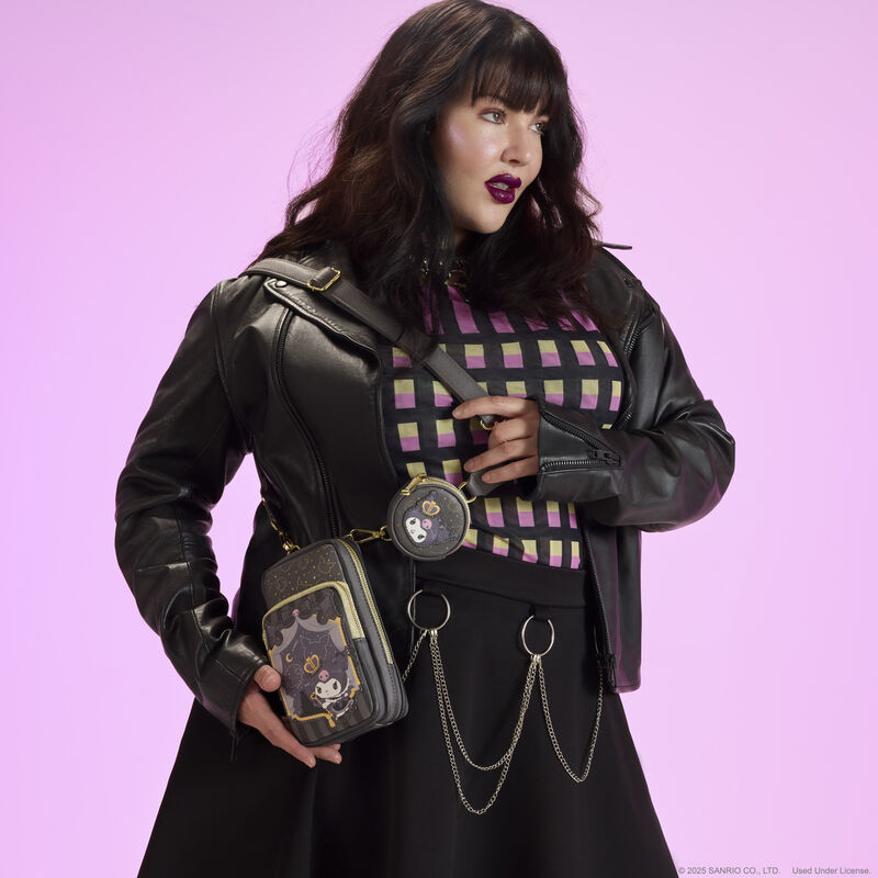 Woman wearing a black, pink, and yellow top and black leather jacket, wearing the Loungefly Kuromi 20th anniversary cellphone crossbody over a shoulder. She stands against a pink-purple background. 
