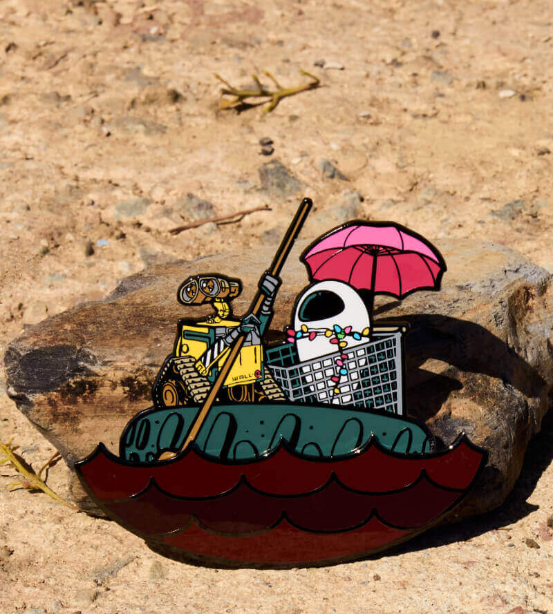 Sand rock textured background with Loungefly Pixar Wall-E Date Night pin. Click to shop pins!